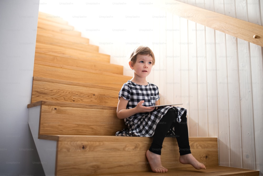 Una bambina seduta all'interno sulle scale, usando il tablet. Copia spazio.
