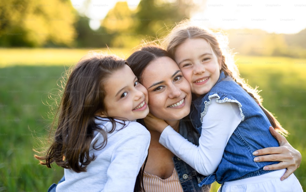 Front view of mother with two small daughters having fun outdoors in spring nature, hugging.