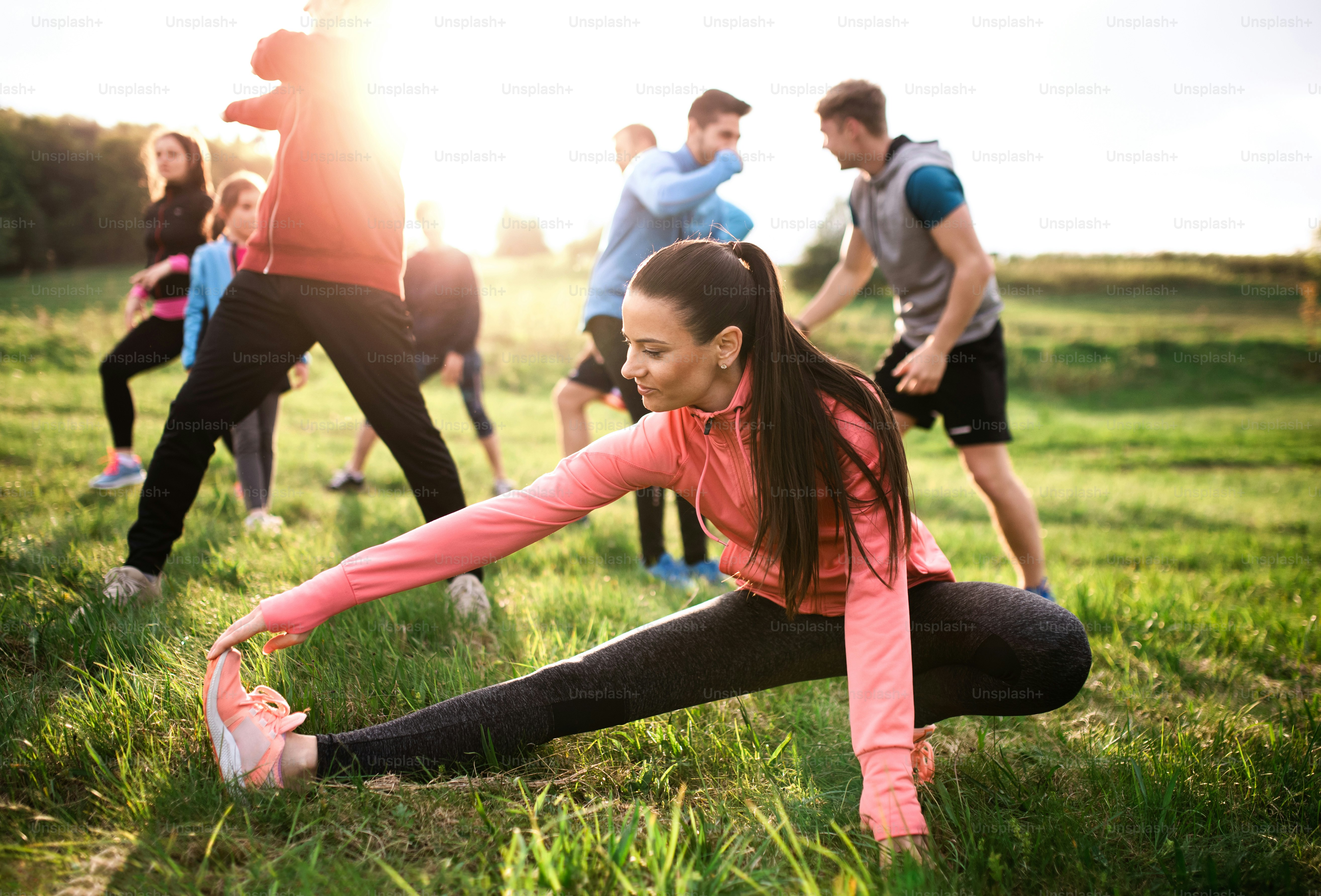 A large group of fit and active people doing exercise in nature, stretching.