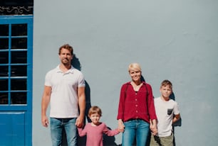 Front view of happy young family with two small children standing outdoors in town.