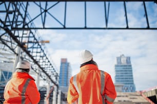 Rear view of engineers or workers standing outdoors on construction site.
