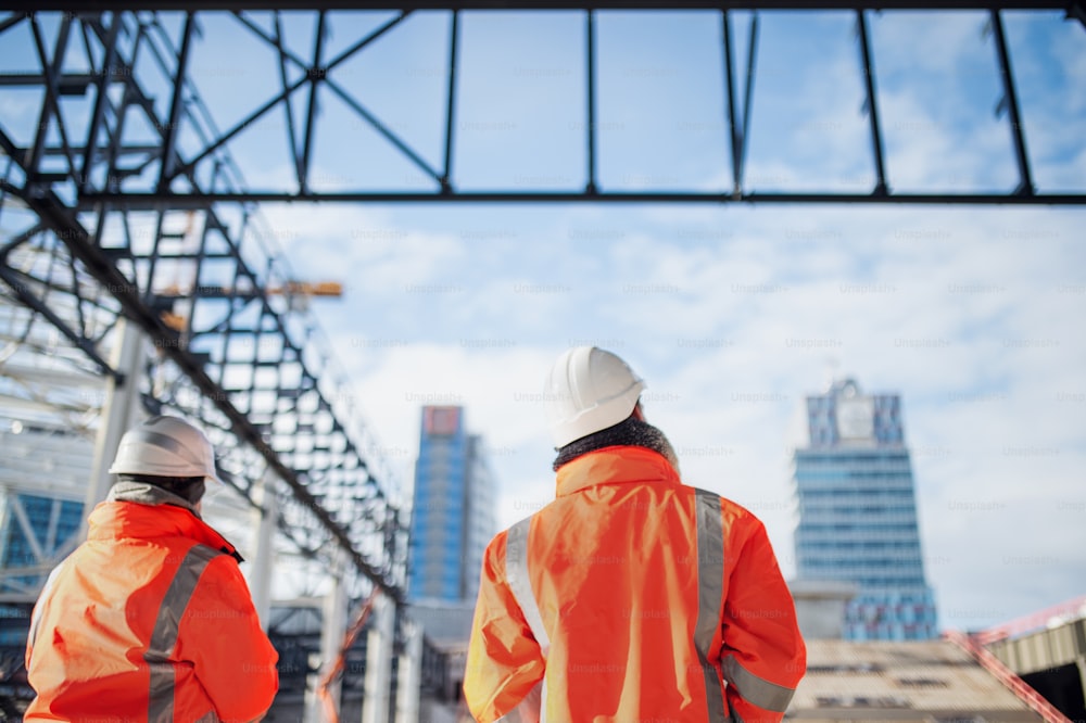 Rear view of engineers or workers standing outdoors on construction site.