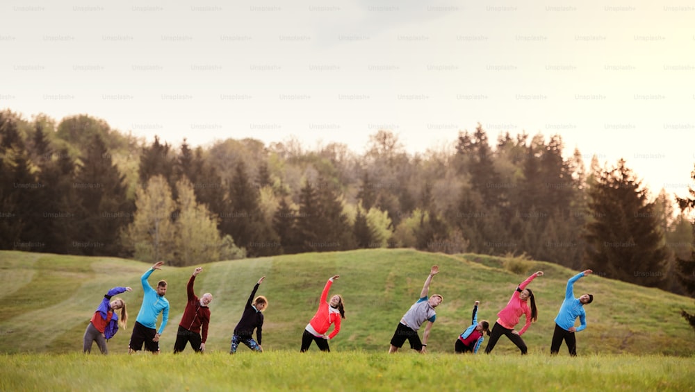 A large group of active multi generation people running a race competition in nature, stretching.