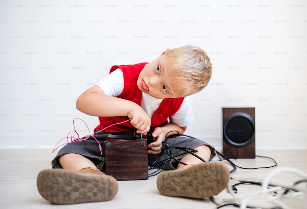 A portrait of happy down-syndrome school boy sitting on the floor, using loudspeakers.