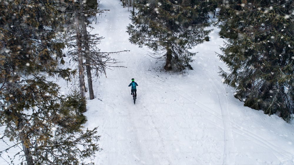 Luftaufnahme eines Mountainbikers, der im Winter im Winter im Wald auf schneebedeckter Straße fährt.