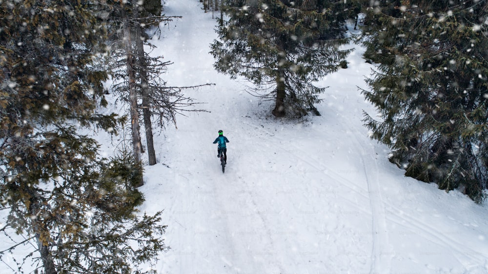 Aerial view of mountain biker riding on road covered by snow in forest outdoors in winter.