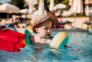 Un niño pequeño feliz con brazaletes nadando en el agua en vacaciones de verano.