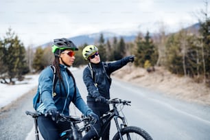 Two mountain bikers riding on road outdoors in winter, talking.
