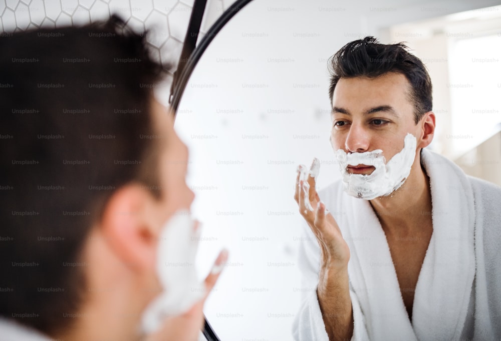 Young man with shaving foam on face in the bathroom in the morning, a daily routine.