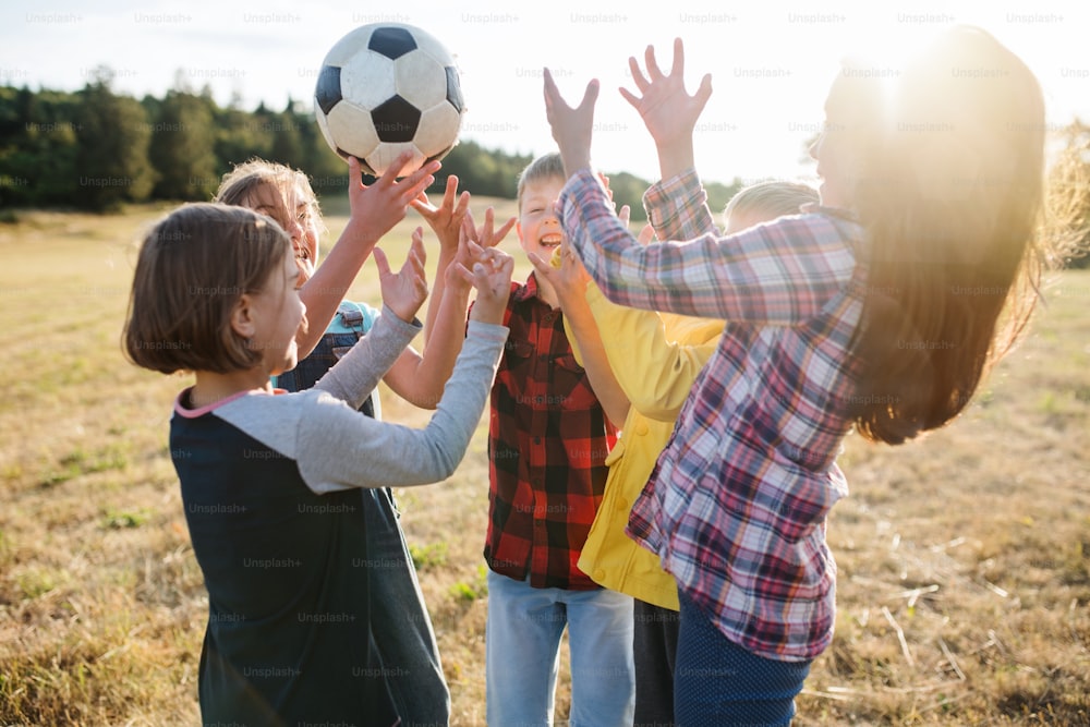 Porträt einer Gruppe von Schulkindern, die auf Exkursion in der Natur stehen und mit einem Ball spielen.