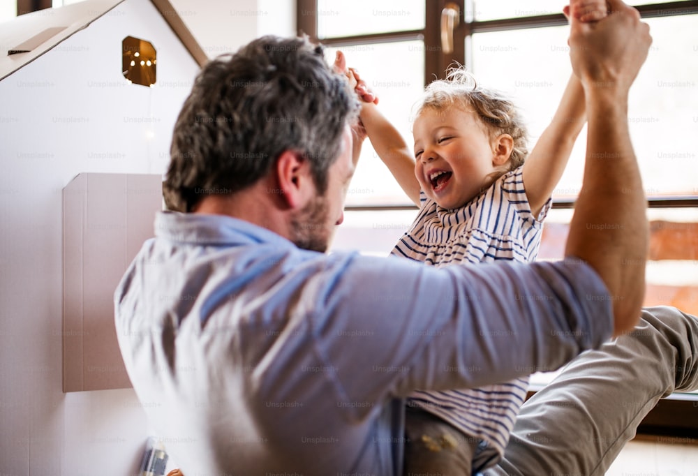 Duas crianças pequenas felizes com um pai e uma casa de papelão brincando dentro de casa.