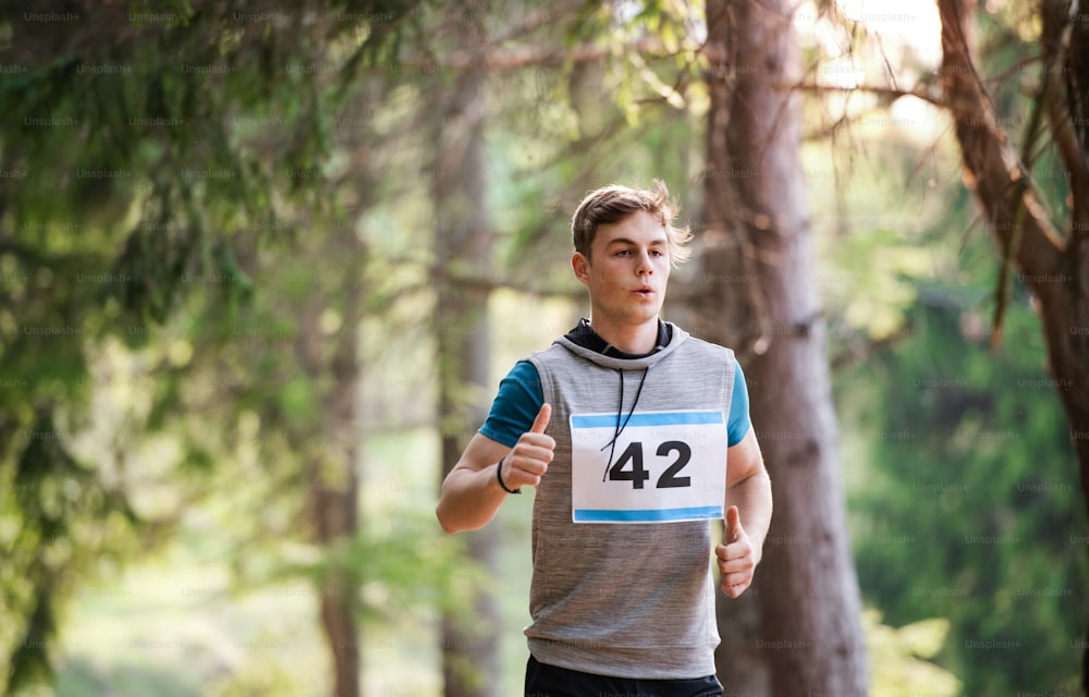 A front view of young man running a race competition in nature. Copy space.