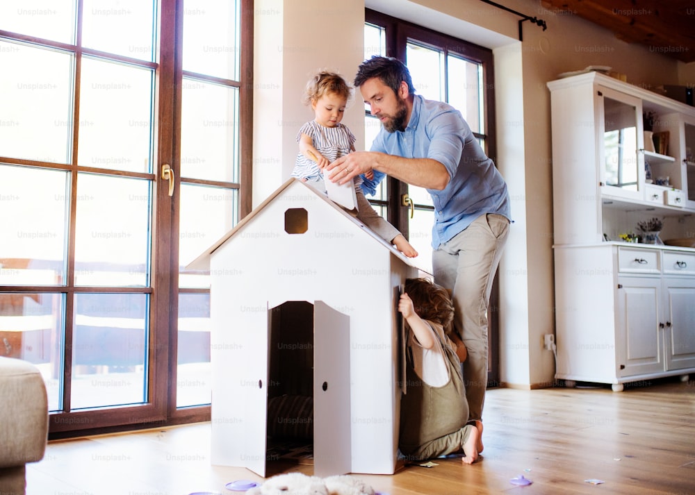 Duas crianças pequenas felizes com o pai brincando com a casa de papel dentro de casa.