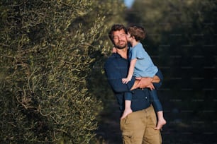 Pai feliz com filha pequena em pé ao ar livre pela oliveira, beijando.