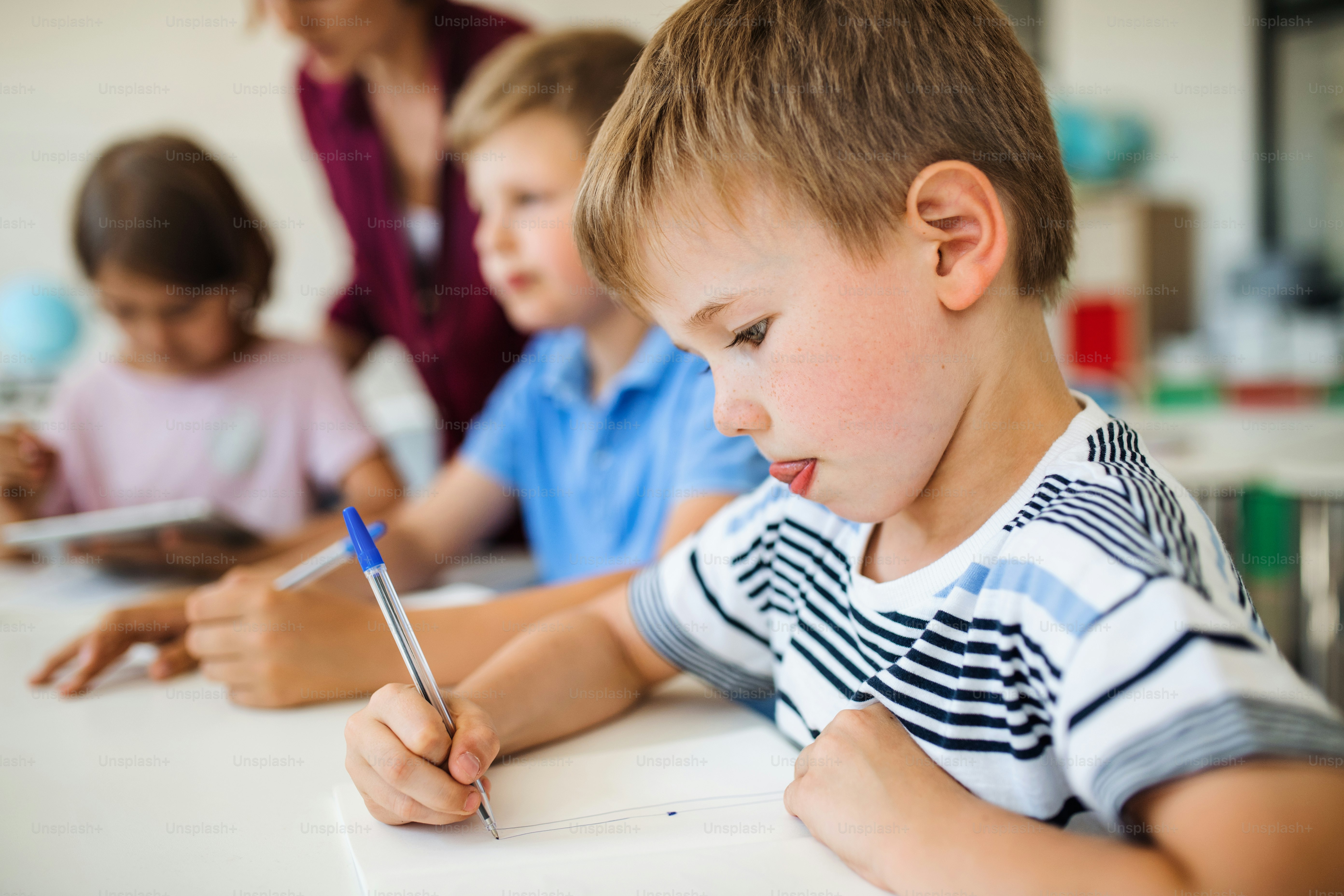 Sekelompok anak sekolah kecil dengan guru duduk di meja dalam menulis kelas.