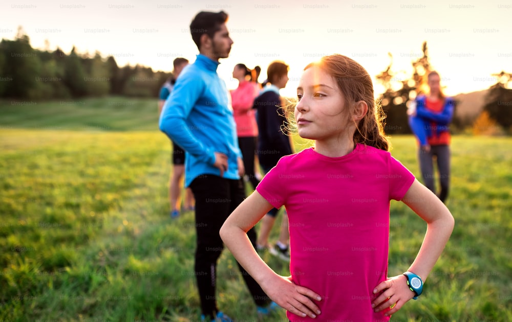 A portrait of small girl with large group of people doing exercise in nature, resting.