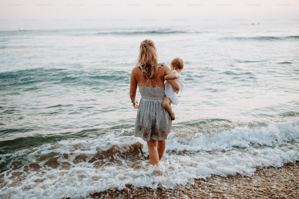 A rear view of young mother with a toddler girl walking in sea on summer holiday.