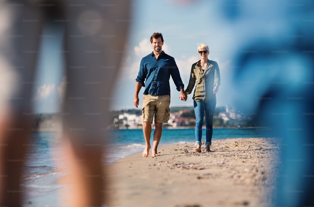 Young happy couple walking outdoors on beach, holding hands.