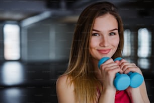 A portrait of happy young girl or woman with dumbbells in a gym. Copy space.