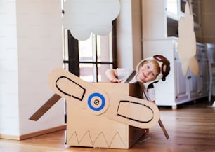 Un niño pequeño feliz con un avión de cartón que juega en el interior de casa, concepto de vuelo.