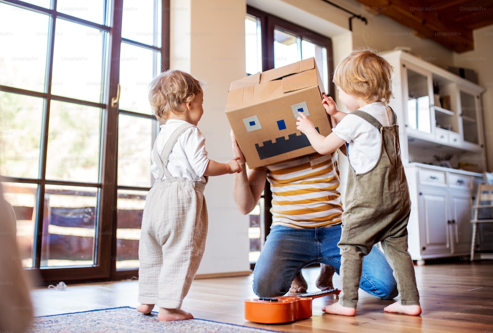Dos niños pequeños felices con un padre y un monstruo de cartón jugando en el interior de la casa.