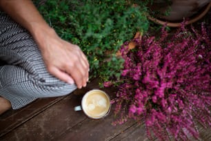 A midsection of woman with coffee sitting outdoors on terrace, resting.