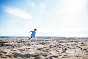 A small happy girl running outdoors on sand beach. Copy space.