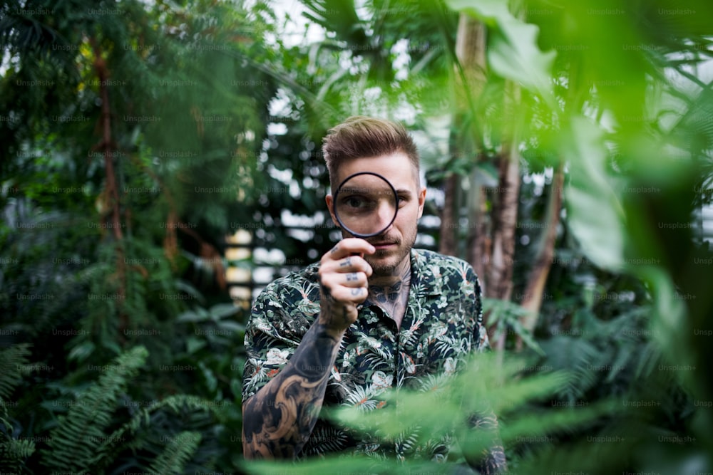 Young man researcher with magnifying glass standing in botanical garden.