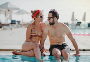 A cheerful couple in swimsuit sitting by the swimming pool on summer holiday.