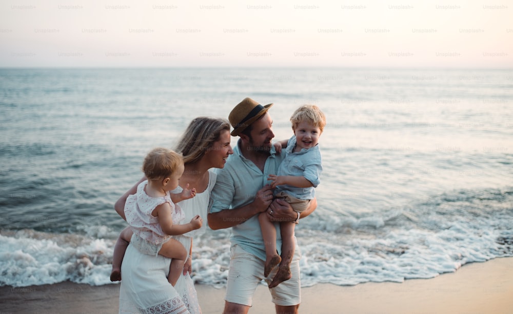 Une jeune famille avec deux enfants en bas âge debout sur la plage pendant les vacances d’été, riant.
