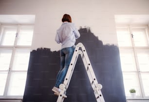 Uma visão traseira da jovem mulher criativa pintando a parede preta. Uma startup de pequenas empresas.