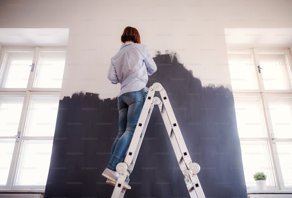 Una vista trasera de una joven mujer creativa pintando la pared de negro. Una startup de pequeña empresa.