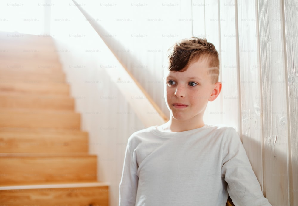 A small boy standing indoors by the wooden stairs. Copy space.