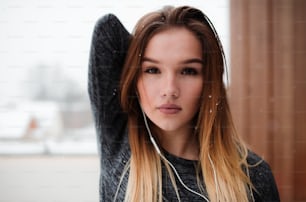 A portrait of young girl or woman with earphones doing stretching outdoors on a terrace. Copy space.