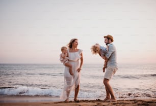 A young family with two toddler children standing on beach on summer holiday, having fun.