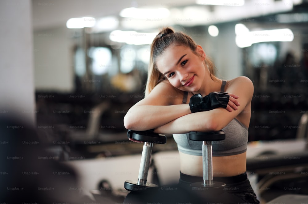 Ein junges Mädchen oder eine junge Frau mit Hanteln, die in einem Fitnessstudio trainieren.