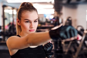 Una vista frontal de una niña o mujer joven con guantes, haciendo ejercicio en un gimnasio.
