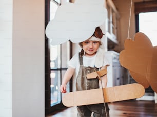 Un niño pequeño con un avión de cartón y nubes jugando en el interior de casa, concepto de vuelo.
