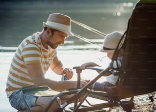 Un padre maduro con un hijo pequeño pescando al aire libre junto a un río o un lago, hablando.