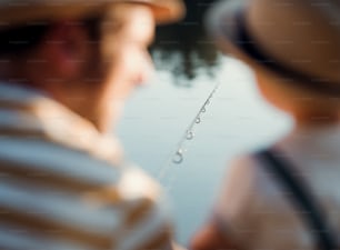A rear view of mature father with a small toddler son outdoors fishing by a river or a lake. A close-up.