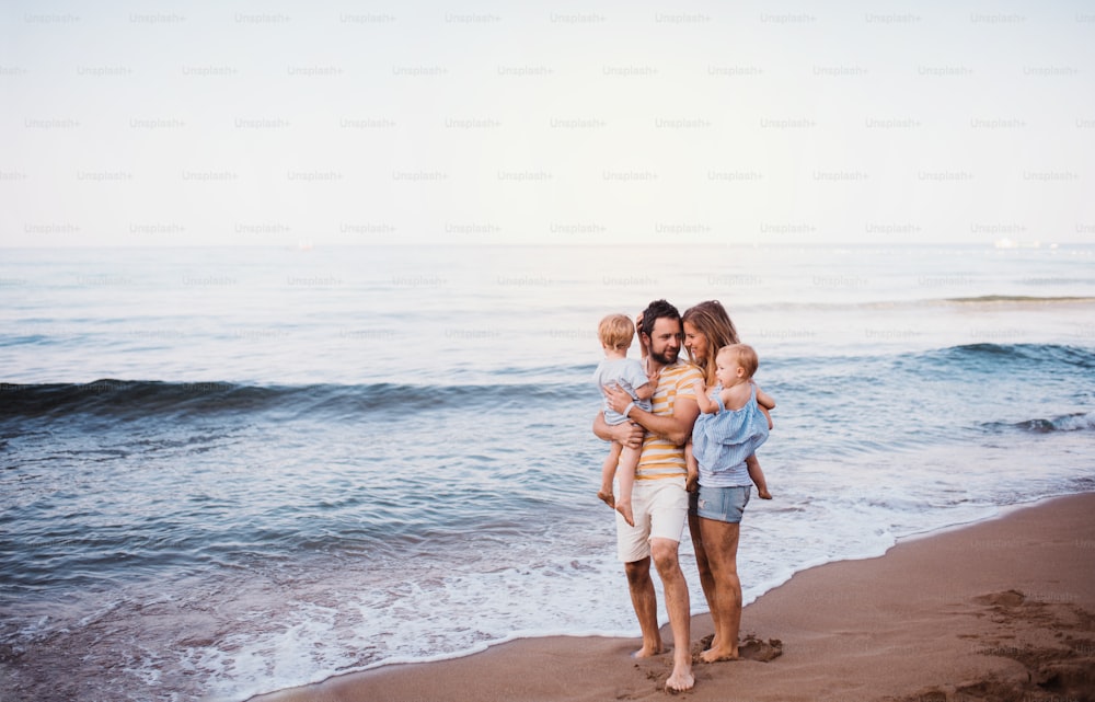Una familia joven con dos niños pequeños de pie en la playa durante las vacaciones de verano. Espacio de copia.