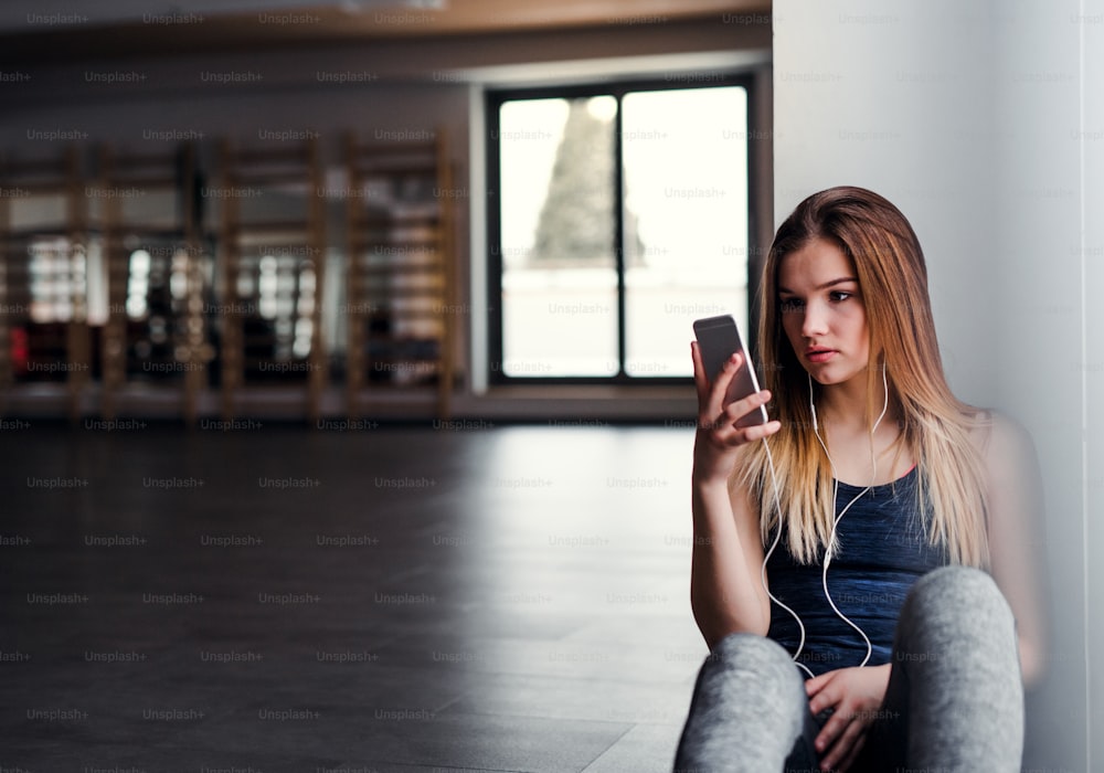 Une jeune fille ou une jeune femme avec des écouteurs et un smartphone dans une salle de sport, écoutant de la musique.