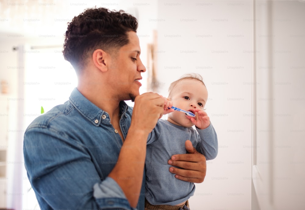 Young father and small toddler son in a bathroom indoors at home, brushing teeth.