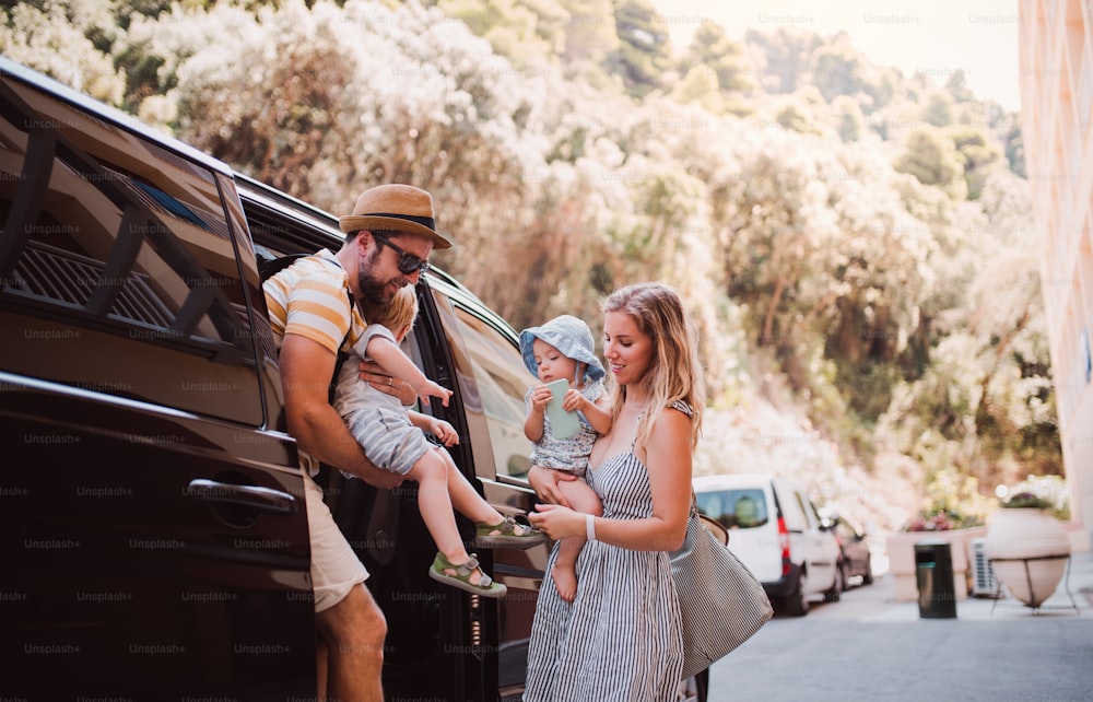 Uma jovem família com duas crianças pequenas saindo do carro de táxi nas férias de verão.