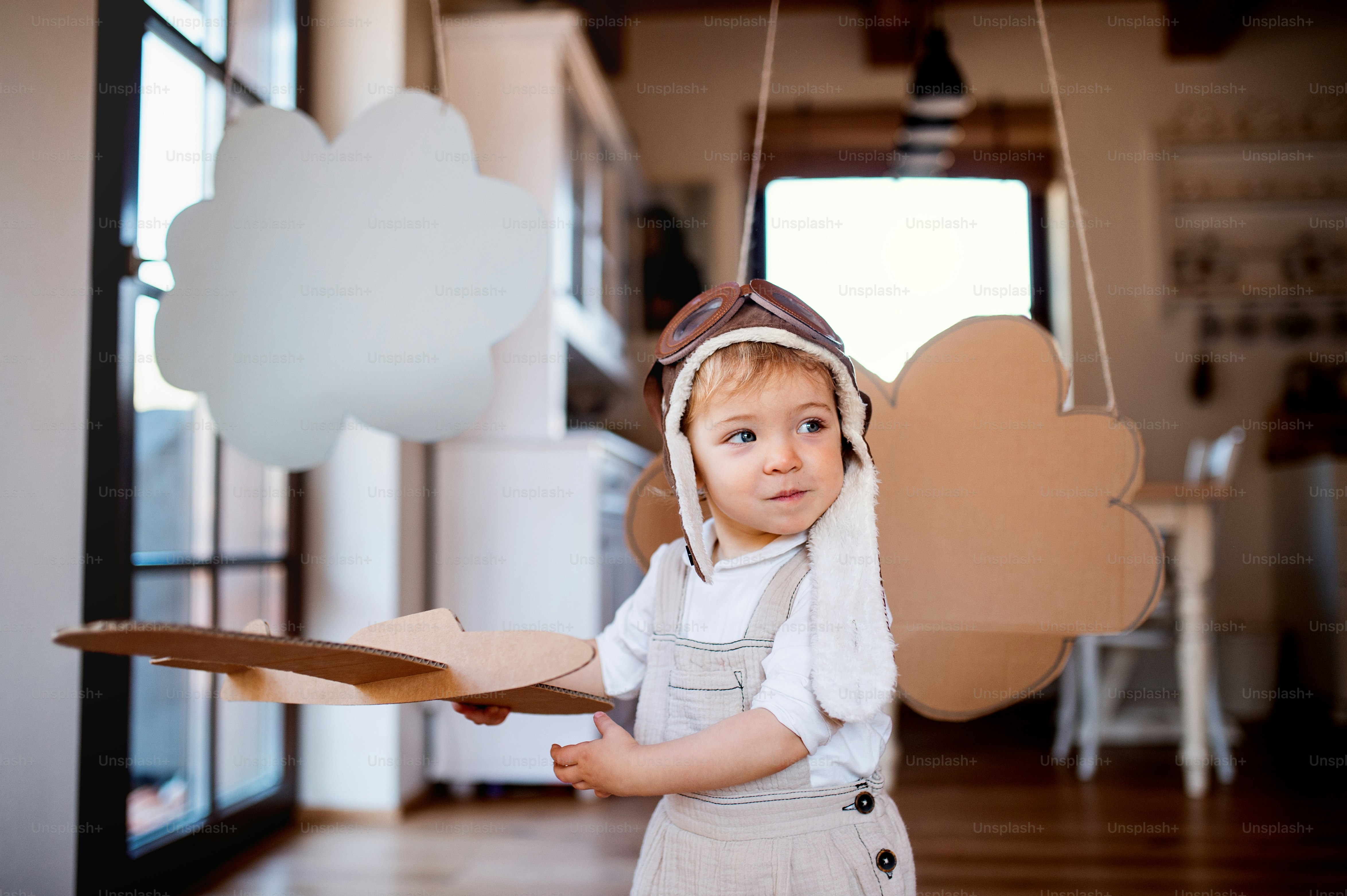 A toddler girl with carton plane and clouds playing indoors at home, flying concept.