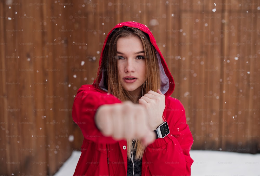 Un ritratto di giovane bella ragazza o donna con smartwatch che fa esercizio all'aperto in inverno.