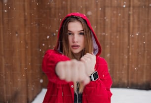 A portrait of young beautiful girl or woman with smartwatch doing exercise outdoors in winter.