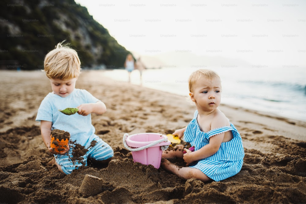 Two toddler children playing on sand beach on summer family holiday.