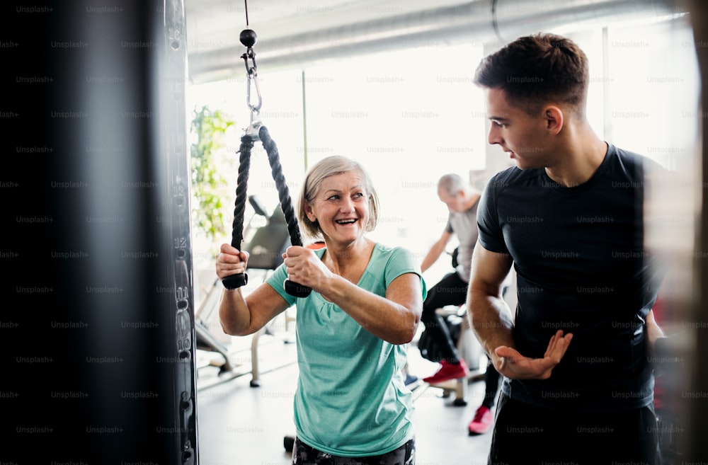 Uma idosa alegre com um jovem treinador fazendo exercícios de treino de força na academia.
