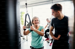 Eine fröhliche Seniorin mit einem jungen Trainer, der Krafttraining im Fitnessstudio macht.